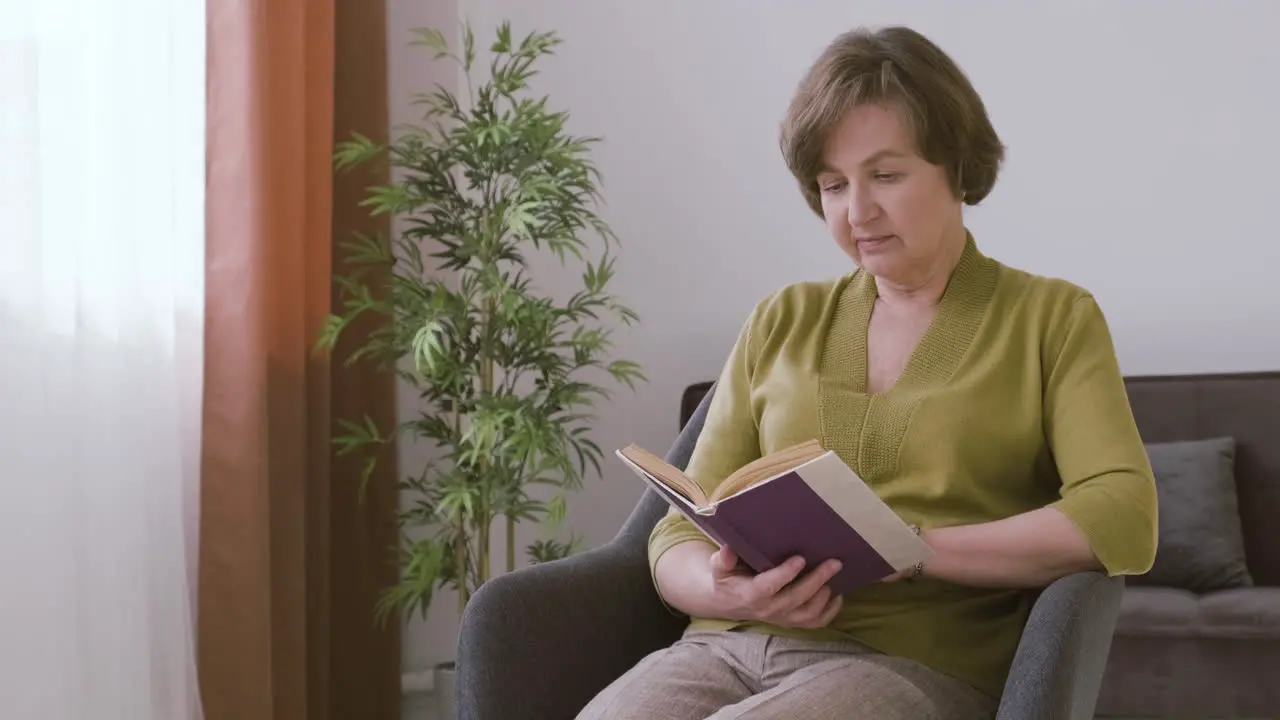 Senior Woman With Gray Hair Sitting On A Sofa Reading A Book