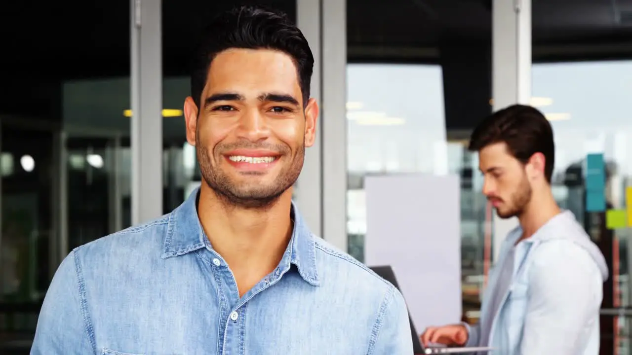 Portrait of male executive using mobile phone with his colleague in background