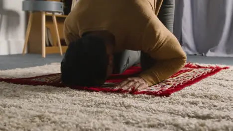 Muslim Man At Home Kneeling On Prayer Mat And Praying