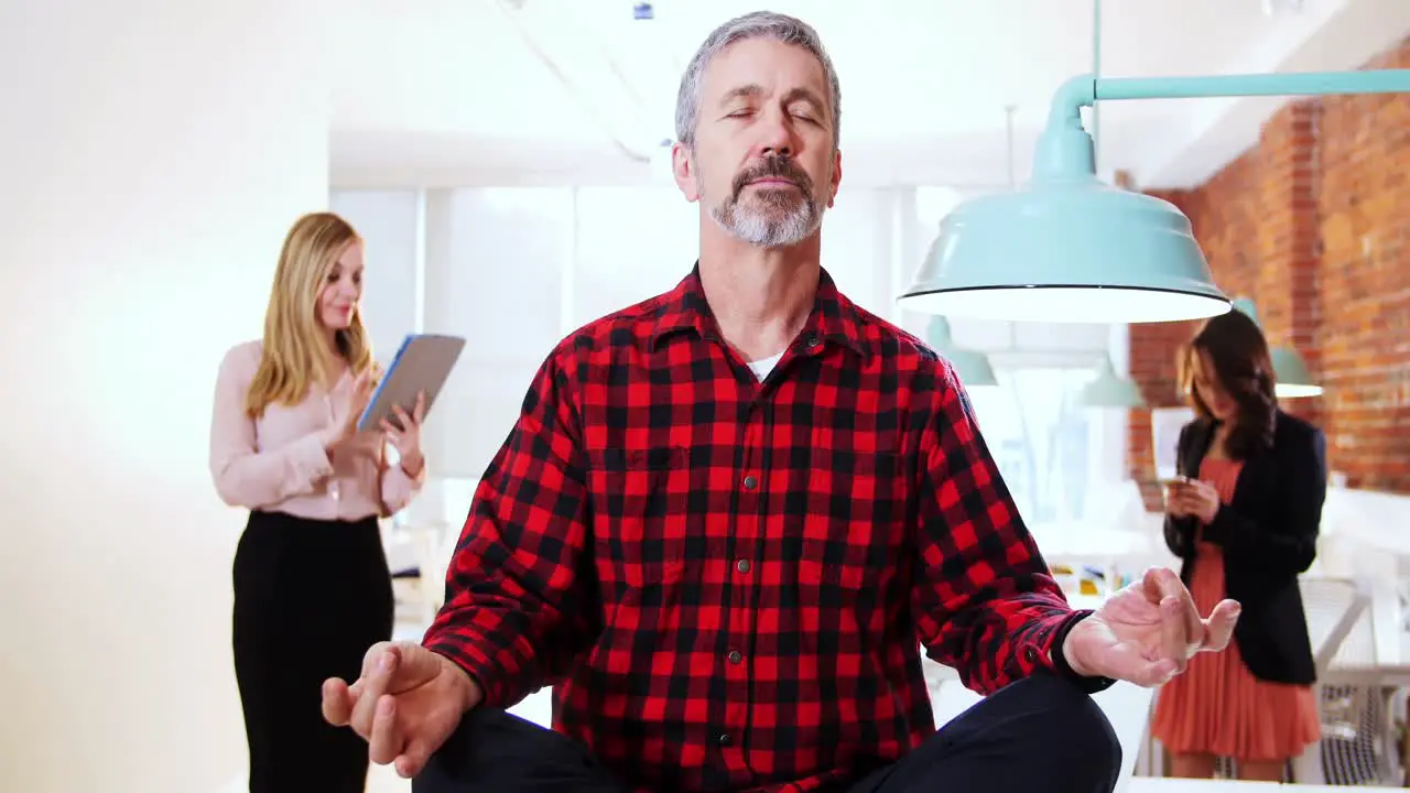 Male executive performing yoga while his executive standing in background