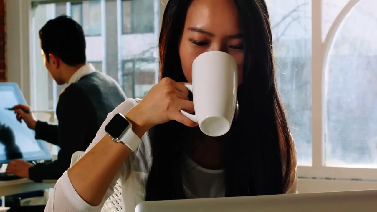 Female executive using laptop while having coffee