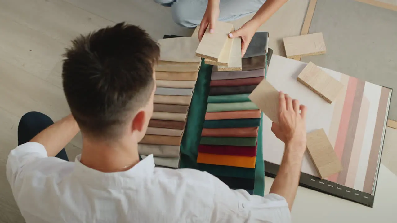 A young couple picks up fabric and wallpaper to repair their home Compare samples of wood fabric and wallpaper