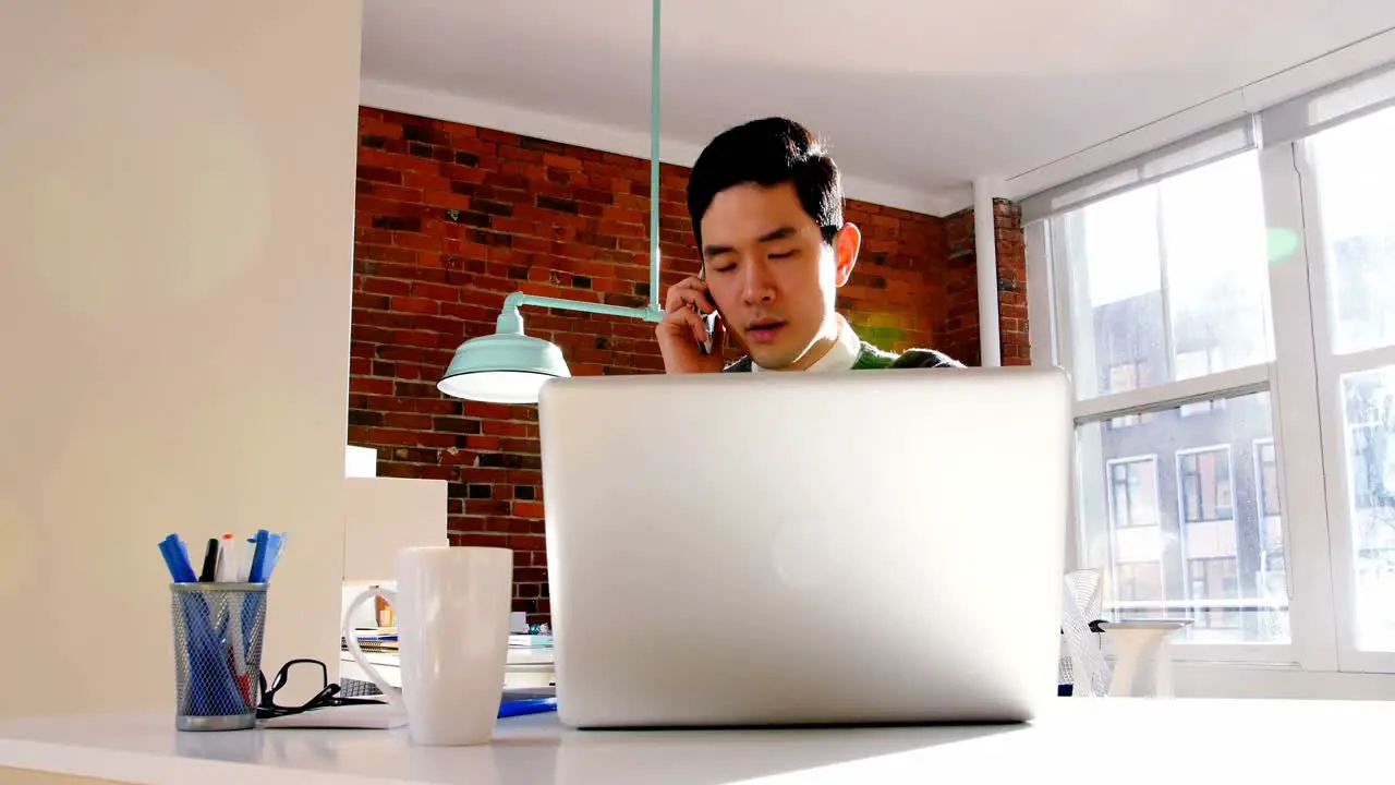 Male executive talking on mobile phone while using laptop