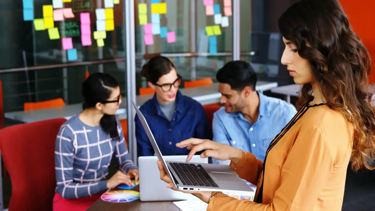 Female executive using laptop while colleagues discussing during meeting