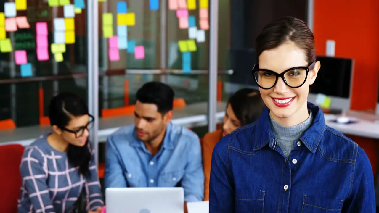 Smiling female executive using digital tablet while colleagues discussing over laptop