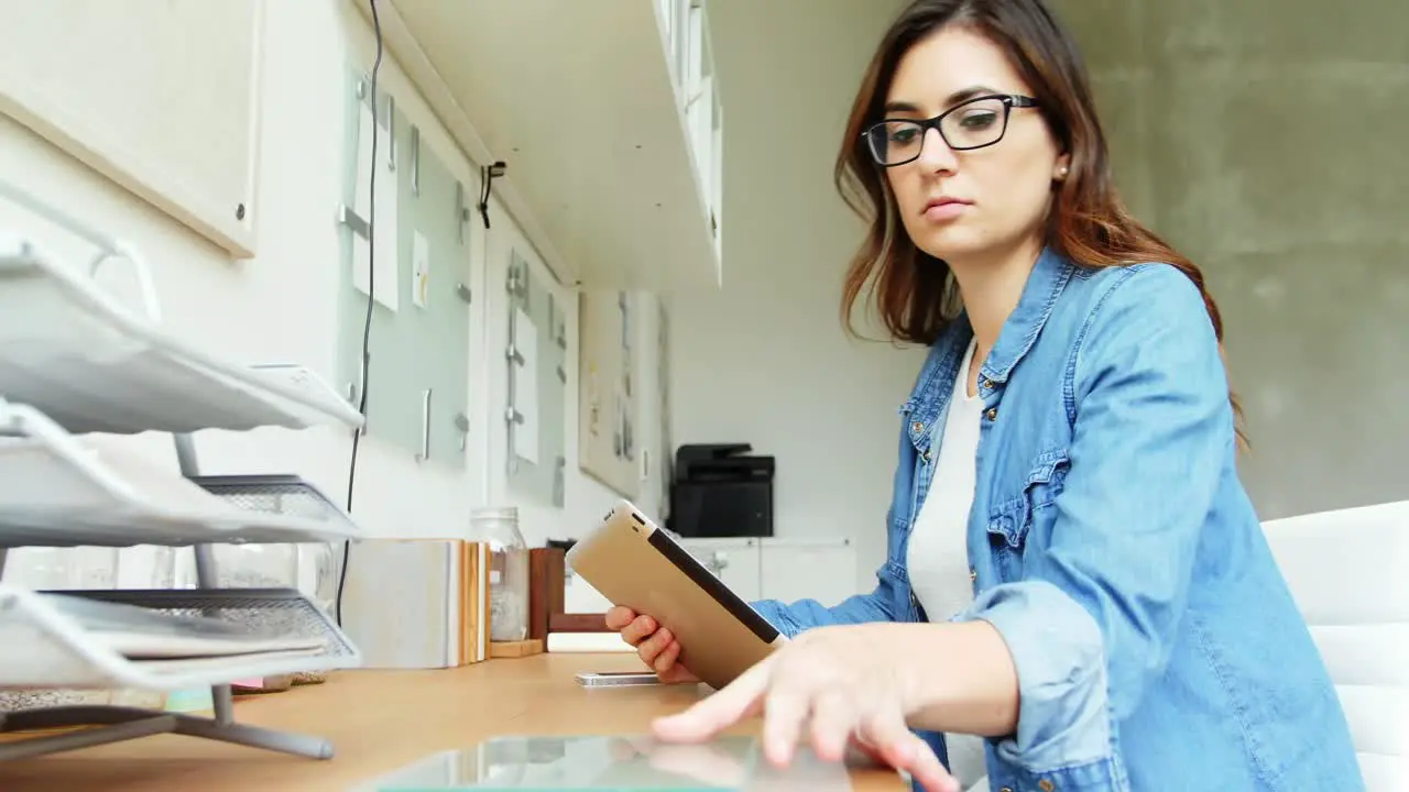 Female executive looking at glass sheet while using digital tablet