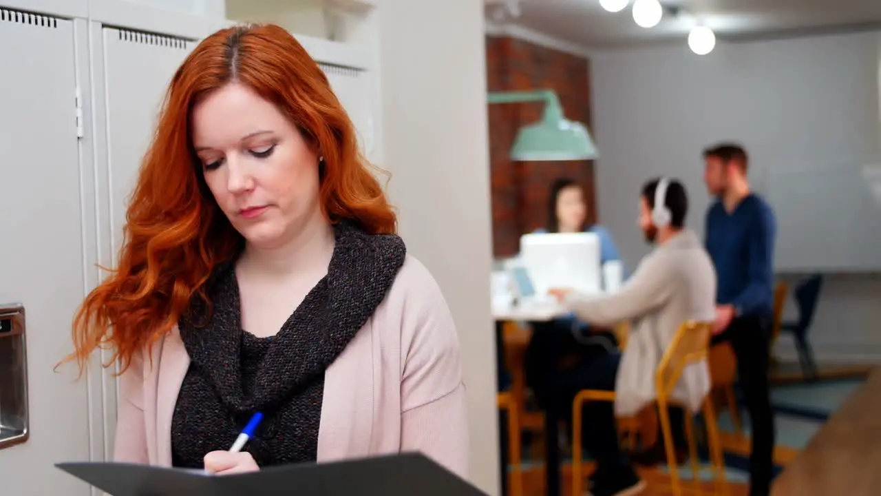 Female executive writing in file in locker room