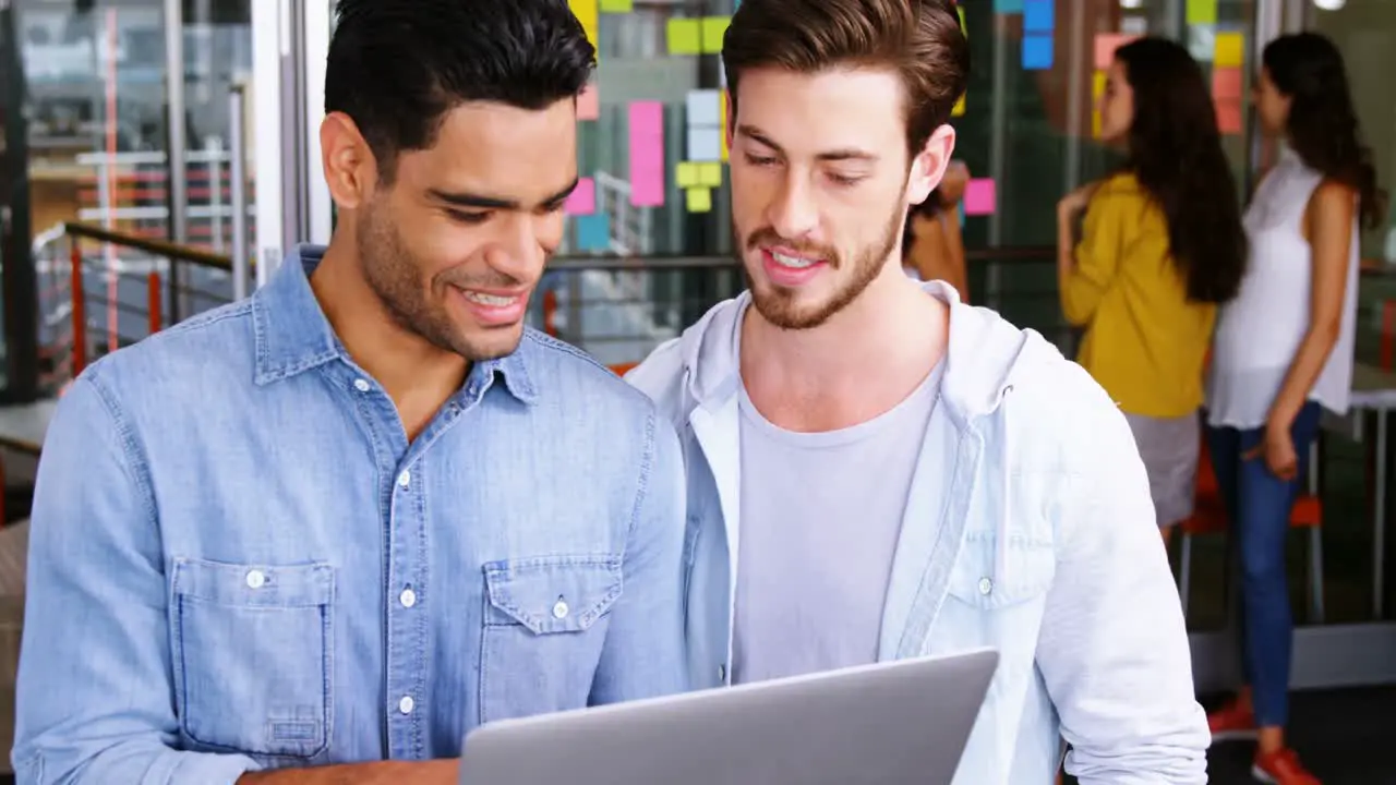 Male executives shaking hands while using laptop