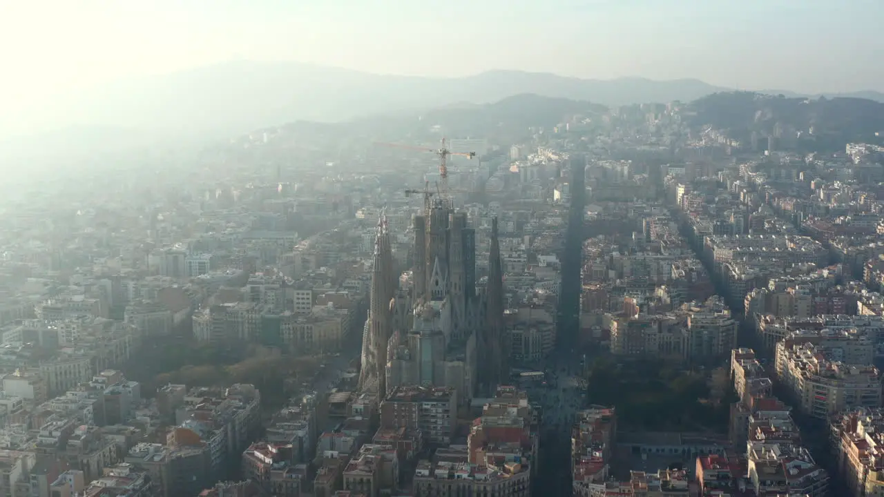 Aerial footage of basilica Sagrada Familia Large unfinished church with tower cranes Hazy view against sun Barcelona Spain