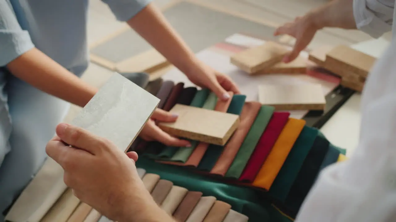 The hands of two designers sorting and comparing samples of fabric wood wallpaper and plaster