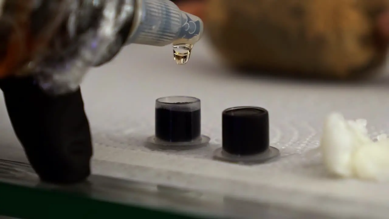 Slow motion close up handheld shot of a tattoo artist adding clear ink to small containers full of blank ink to create a grey color for shading to prepare for a client session