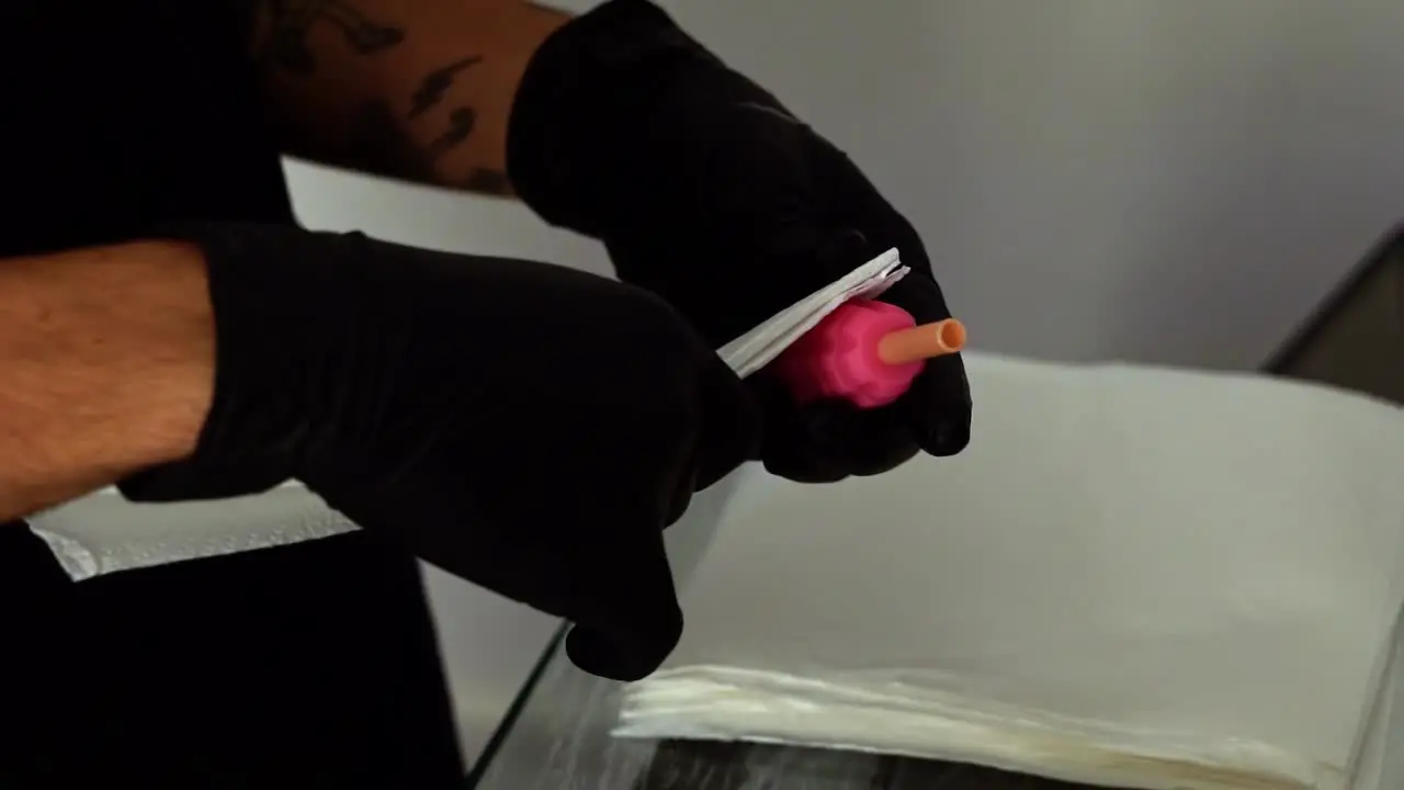 Close up slow motion handheld shot of the hand of a tattoo artist picking up tools from a sanitized table to prepare their needle gun tool for a client session