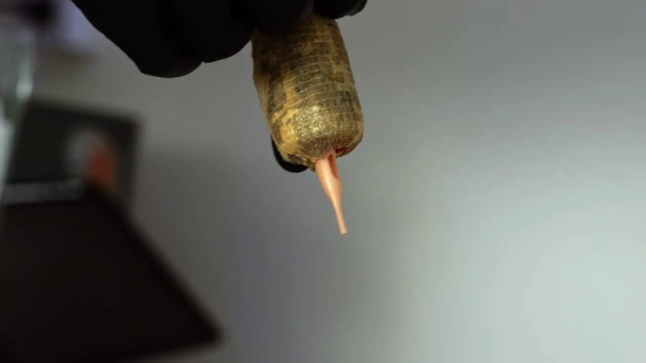 Close up slow motion handheld shot of the hand of a tattoo artist preparing their needle gun tool for a client session by wrapping on tape to create a hand hold