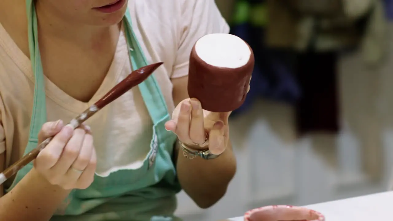 Close up of a woman painting ceramic pieces with a brush in a workshop during the day