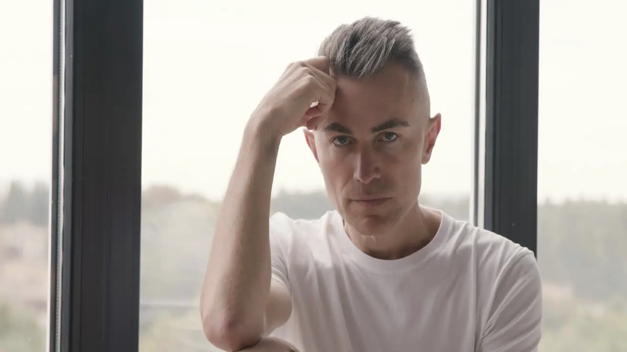 Portrait Of A Pensive Man Sitting By The Window And Looking At Camera