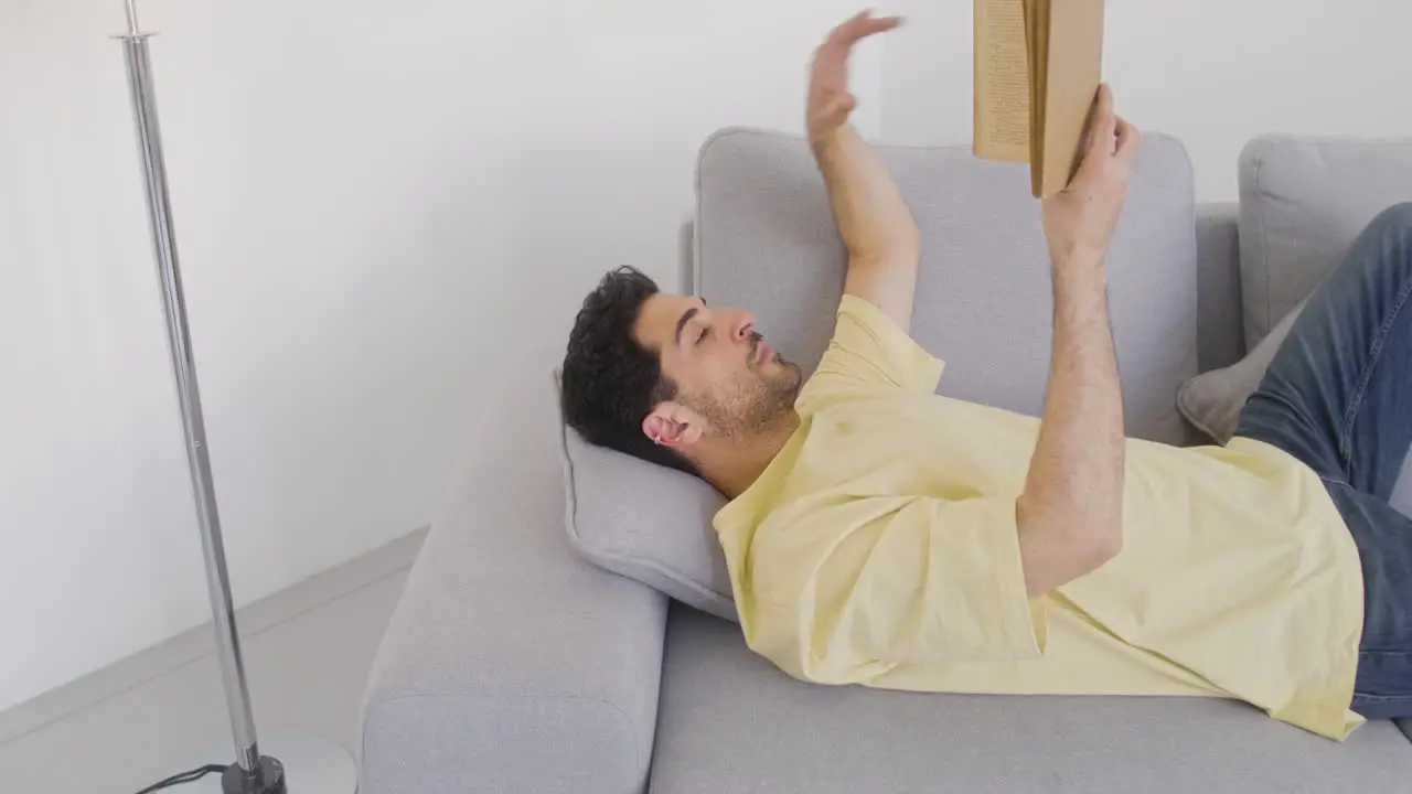 A Dark Haired Man Reads A Book While He Rests On A Sofa