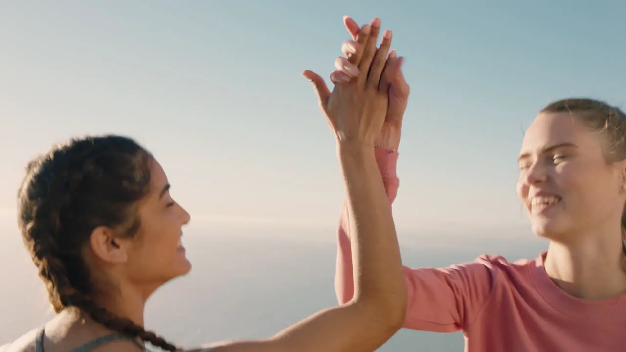 two women friends high five celebrating success climbing mountain on hiking challenge having fun outdoor adventure achievement