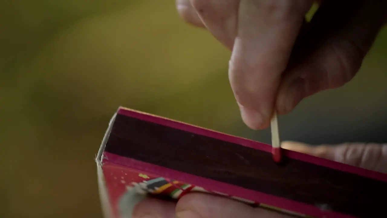 Close up of unidentified hand striking matchstick over matchbox to ignite it