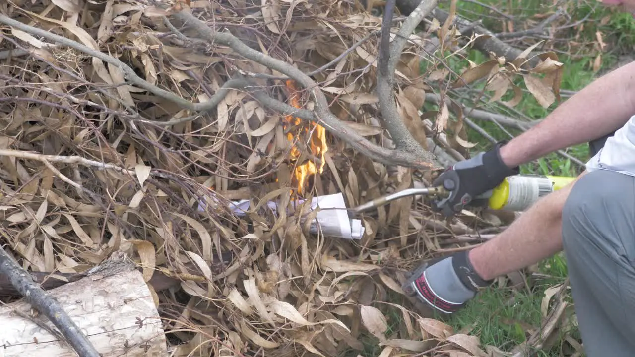 A close up shot of a man starting a bonfire with a gas lighter