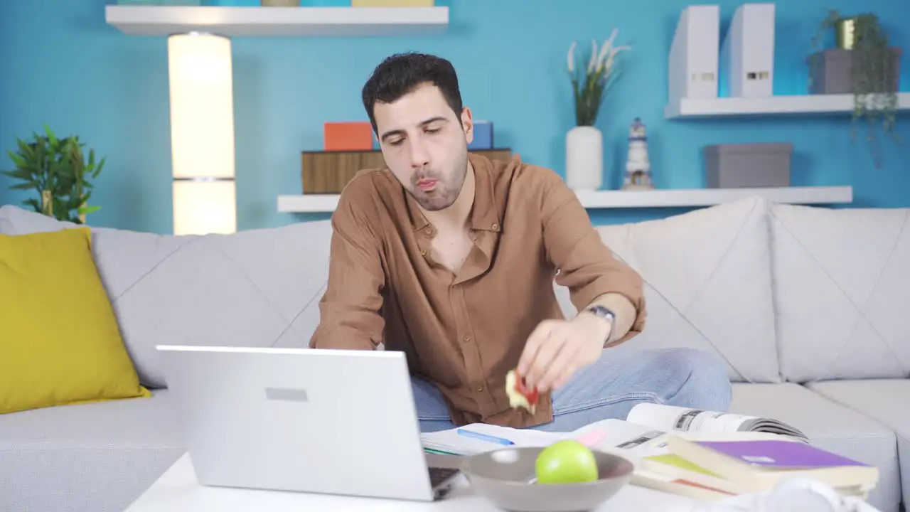 Happy young man working at home and eating fruit