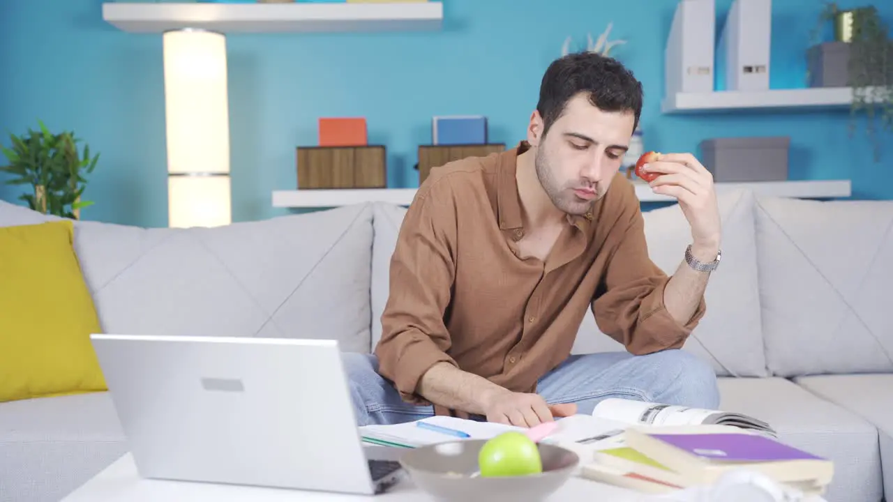 Young man working on laptop at home eating fruit