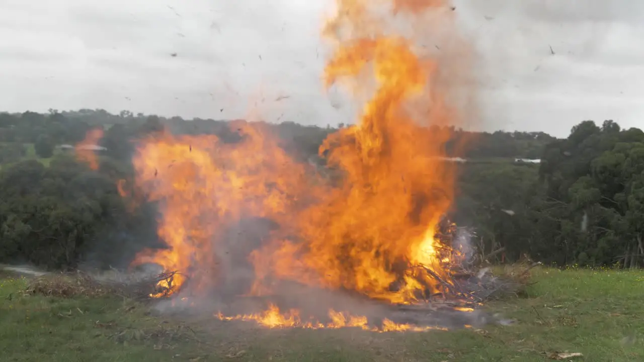 A slow motion shot of a large bonfire on a rural property with ash flying everywhere