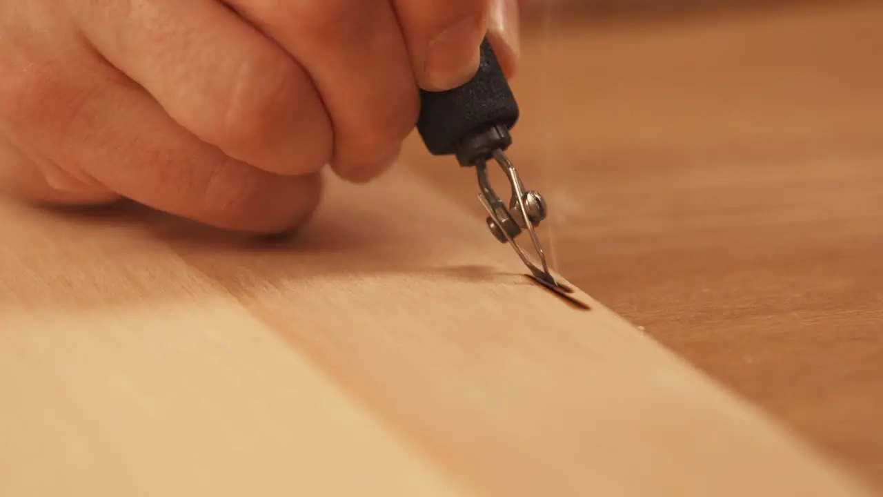 Close up footage of artist woodburning with wisp of smoke releasing from wood burn