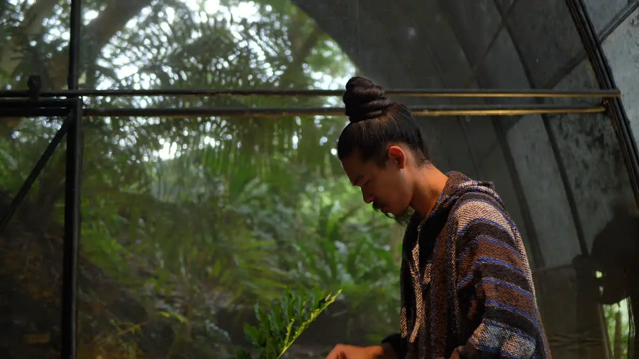 Asian man in hipster clothing lighting a candle with forest in background camera tilting down