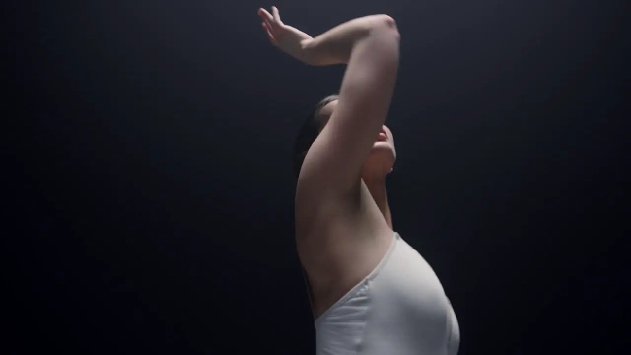 Tender dancer looking upward indoors Beautiful ballerina dancing in dark class