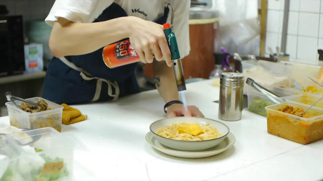 Chef using gas torch to scorch surface of egg and noodle dish in kitchen filmed