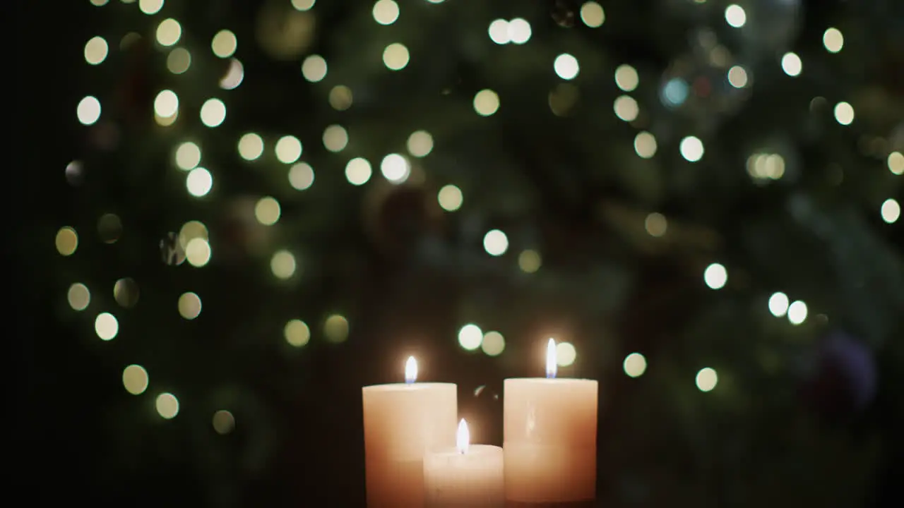 Three candles burn against the backdrop of blurry Christmas tree lights