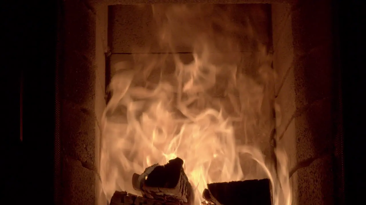 Dolly shot across the inside of a log burning fireplace with high flames bright golden orange flames