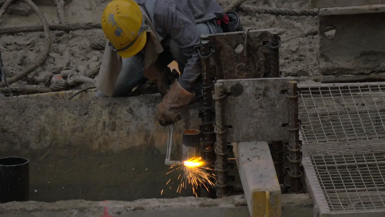 Worker operating with gas jet to cut metal pipe