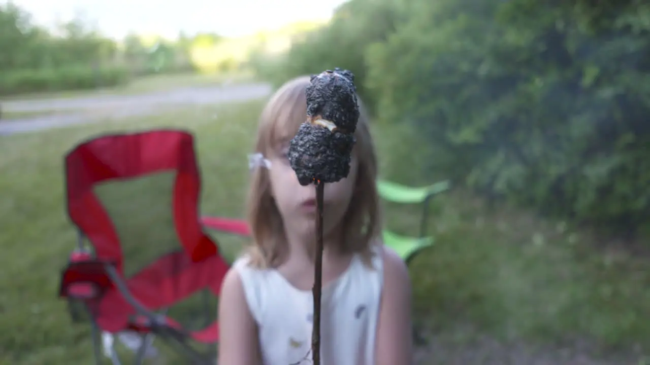 Little girl holding up a burnt marshmallow on a stick