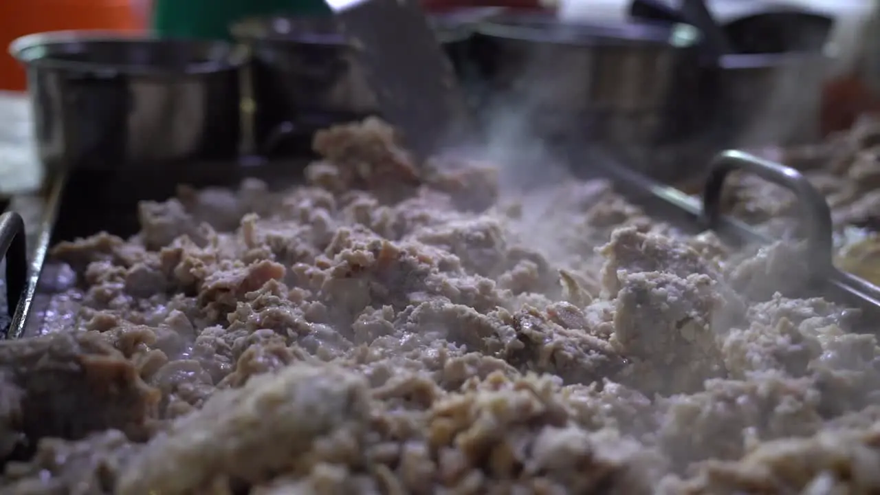 Vendor spreading meat guts with spatula across the griddle in preparation for tacos