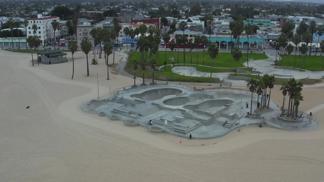 AERIAL Turn around Venice Beach Skatepark with Bikers and Palm trees in morning Cloudy Los Angeles California