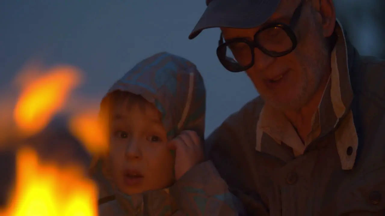 Elderly man sitting with small boy near campfire