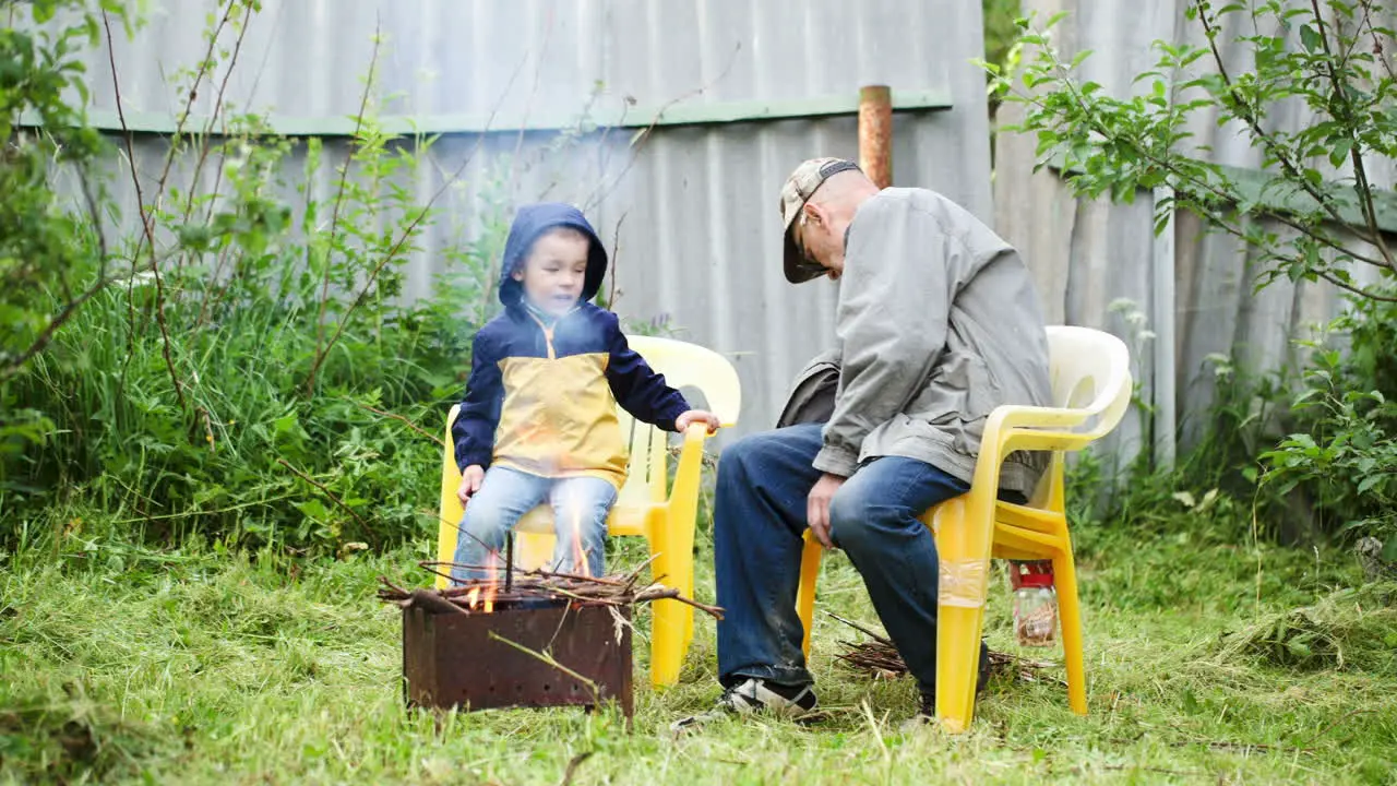 Grandfather and his grandson sitting by the fire outdoor