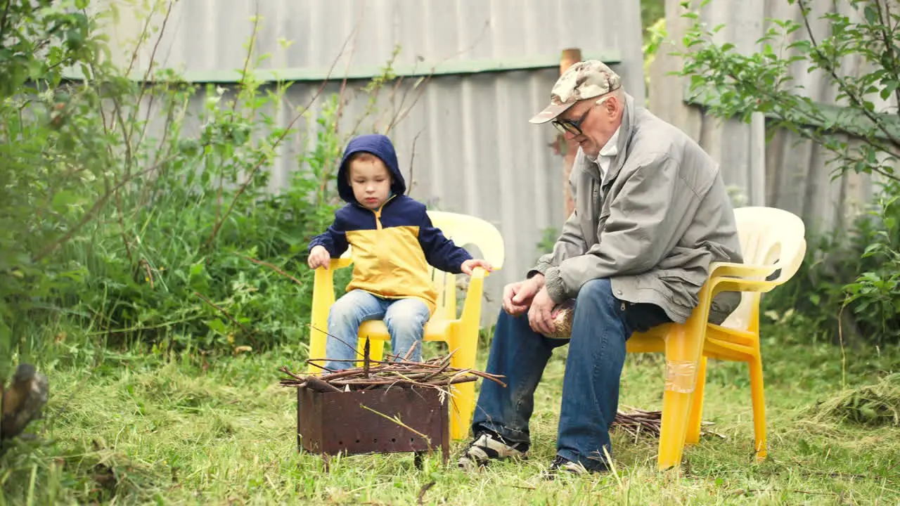 Grandson and grandfather sitting by fire in the yard