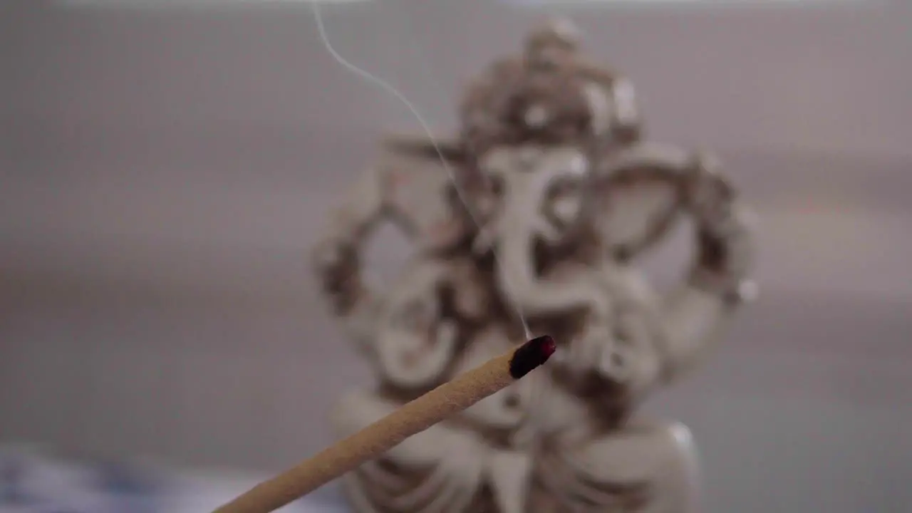 Close-up of a burning incense stick with a Ganesha figure in the background