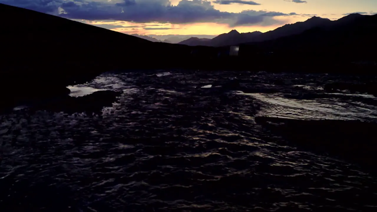 Dark gloomy sunset shot late evening in the mountains with orange and blue sky and a river in the foreground