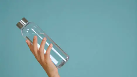 Close Up Shot of Young Womans Hand Bringing Water Bottle into Frame with Copy Space 01