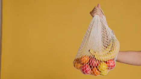 Medium Shot of Young Adult Womans Hand Holding Up Bag of Fruit