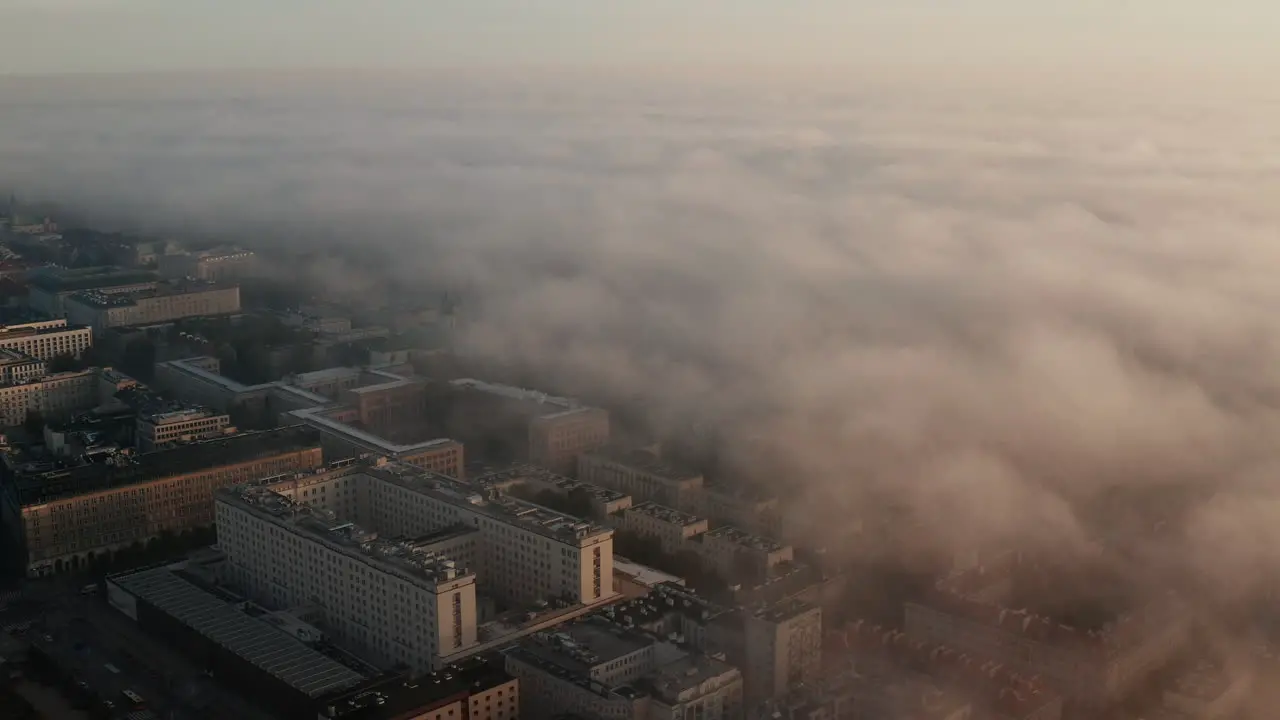 Slide and pan aerial footage of complex of office buildings on edge of fog cover Morning sun glowing into fog Warsaw Poland