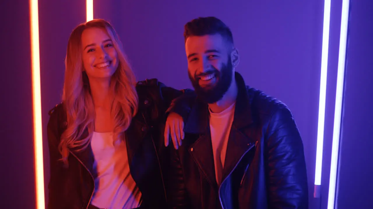 Happy Young Man And Woman Looking At Each Other And Smiling To The Camera On Purple Neon Lights Background