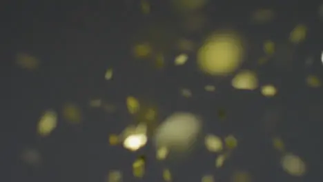 Stationary Shot of Gold Confetti Falling Against a Grey Background