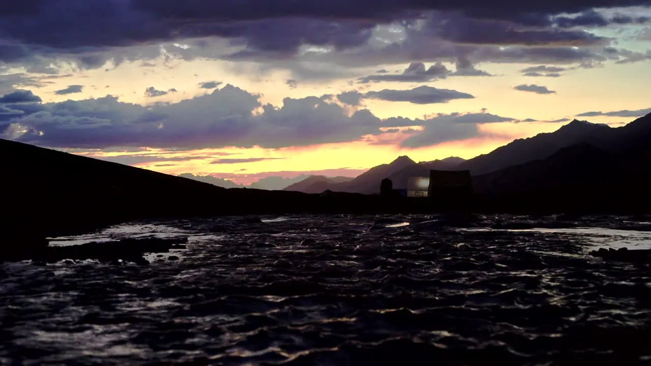 Handheld shot of an amazing sunset in the mountains with orange and blue sky light painting the top of the water of the river running below