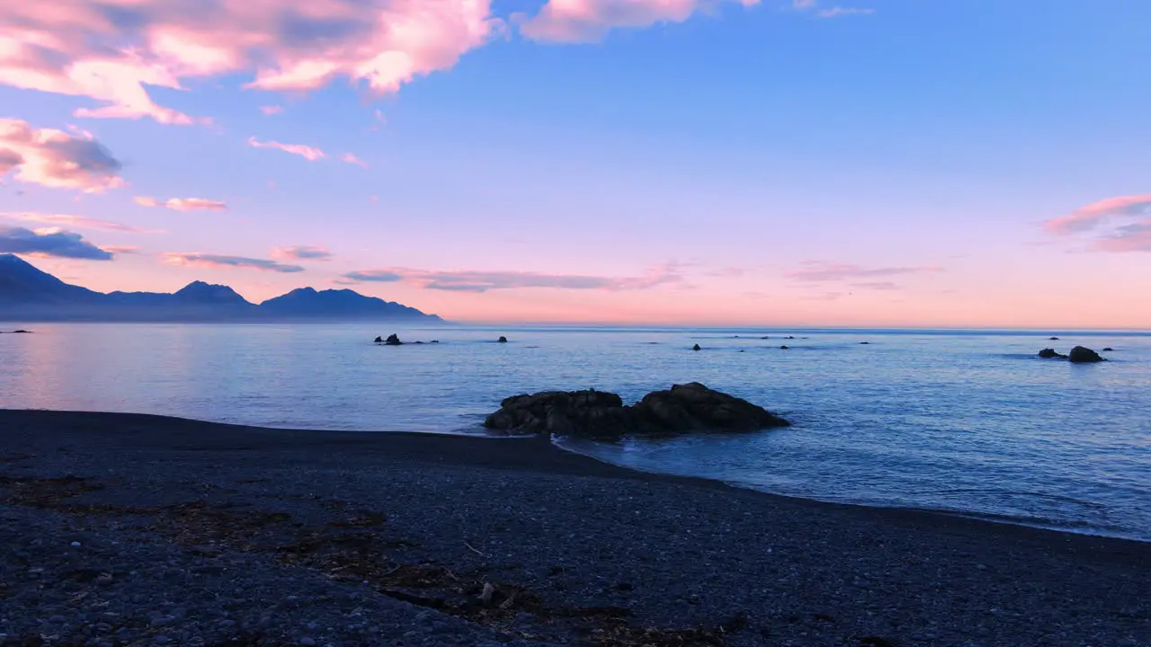 Drone shot of sea with snow capped mountain background and orange sky