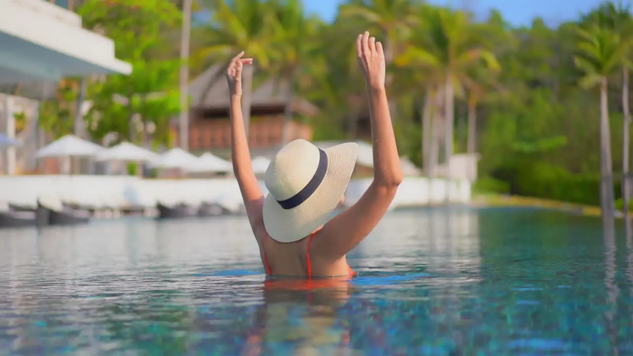 A woman with her back to the camera holds on to the edges of her sun hat as she reacts to the joy of being on vacation