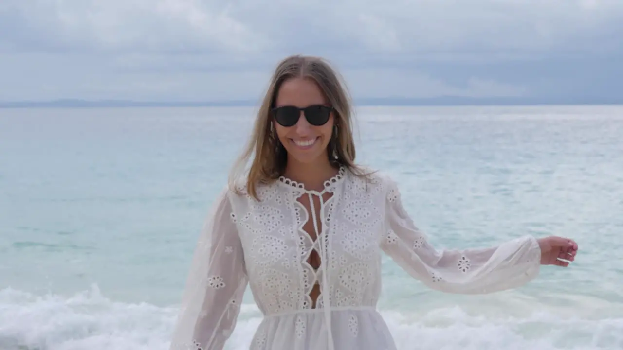 Ultra slow motion shot of happy woman with brown hair in white dress smiling at camera and twirling on beach at Asu Island North Sumatra Indonesia